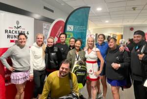 Participants posing in front of tournament flags and banners at the 2022 Tennis Troupe Charity Event